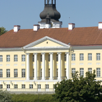 Helekollane sammastega hoone punase katuse ja torniga, ees rohelised puud.