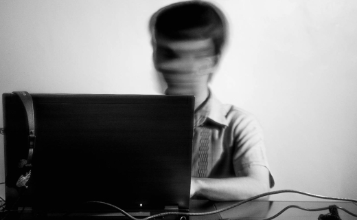 Mustvalge lähikaader sülearvuti taga istuvast inimesest, kelle nägu on tahtlikult hägustatud.